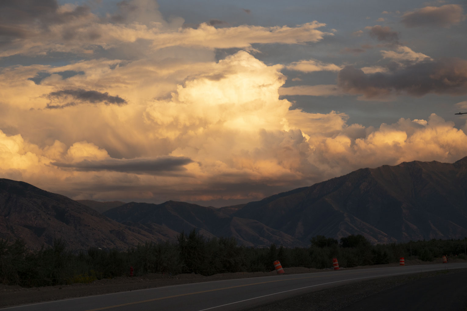 Textured yellow dramatic clouds over the mountains, in the foreground a road and some construction cones